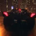 Batmobile speeding through a rainy Gotham City at night with neon reflections, skyscrapers, and dramatic lighting – wallpaper.