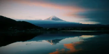 Mount Fuji at sunrise with pastel sky, soft pink and orange clouds, calm reflective lake mirroring the mountain live wallpaper