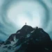 Lone figure standing on snowy mountain peak under massive swirling cosmic vortex sky with dramatic blue tones and atmospheric sci fi landscape wallpaper