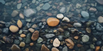 Clear river water over smooth natural pebbles with soft ripples and earthy tones creating calm relaxing nature aesthetic wallpaper