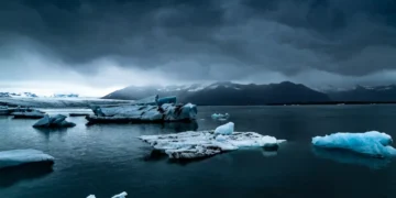 arctic glacier floating ice in calm dark water with mountains and cloudy sky peaceful cold landscape wallpaper