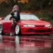 Anime Girl Nissan Silvia Live Wallpaper 10 Pink-haired anime girl leaning on a red Nissan Silvia in a rainy autumn parking lot with reflective wet pavement and cinematic JDM street racing atmosphere wallpaper