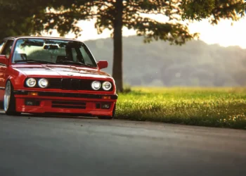Lowered red BMW E30 with deep-dish wheels parked beside a tree during golden hour live wallpaper.