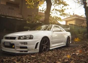 Nissan Skyline GT-R R34 Autumn Live Wallpaper 2 White Nissan Skyline GT-R R34 parked among autumn leaves with warm golden sunlight in a peaceful neighborhood live wallpaper.