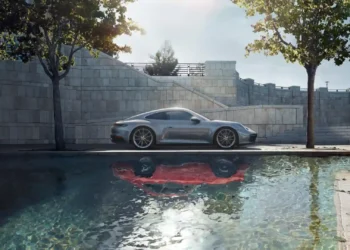 Porsche 911 Carrera Silver Live Wallpaper 1 Silver Porsche 911 Carrera sports car parked beside a reflective pool with modern stone architecture, green trees, and warm sunlight in a Full HD live wallpaper.