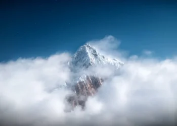 Snowy Mountain Above Clouds Live Wallpaper 1 Majestic snow-covered mountain peak rising above thick white clouds beneath a deep blue starry sky in a peaceful scenic nature live wallpaper.